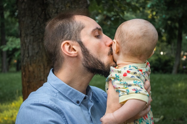 Padre joven con hijo y besarlo en primer plano de la mejilla en el fondo de un paisaje de verano. La ternura del padre hacia su hijo