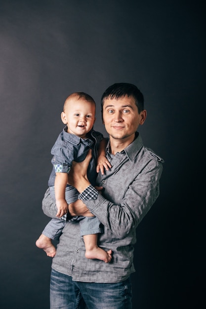 Foto padre joven con hijo pequeño en sus brazos aislado sobre fondo oscuro. familia feliz. dia del padre.