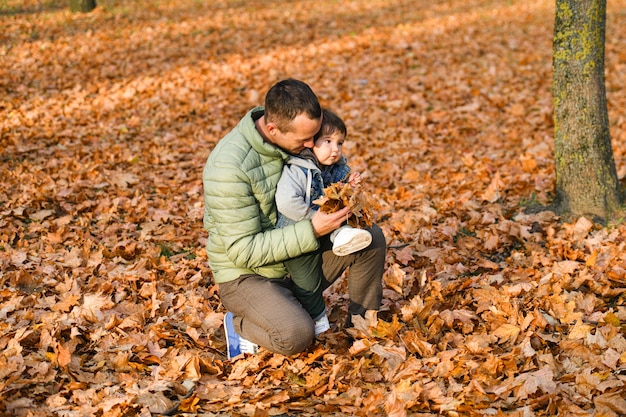 Padre joven jugando con un niño pequeño en un parque de otoño.