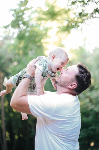 Padre joven y niño pequeño posando positivamente en la naturaleza durante el cálido momento del día