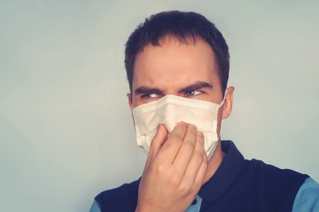 Padre joven que sostiene el pañal sucio sucio en los dedos de una mano con máscara de gas sobre fondo blanco. Olor desagradable hedor. mala ecología, contaminación por gas