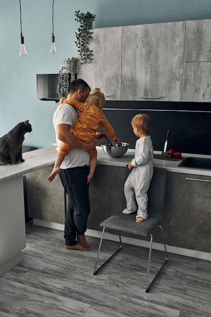 Un padre joven con sus mellizos, de tres años, un niño y una niña, están preparando la comida en la cocina. Familia, hijos, concepto de paternidad. Dia del padre. Estilo de vida.