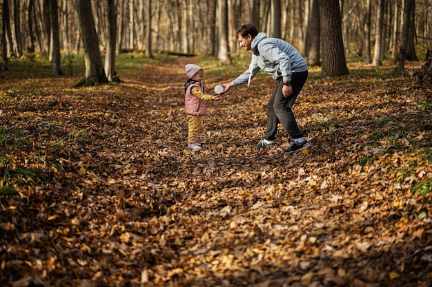 Padre juega con su hija en el ocio familiar en la actividad de otoño en el bosque