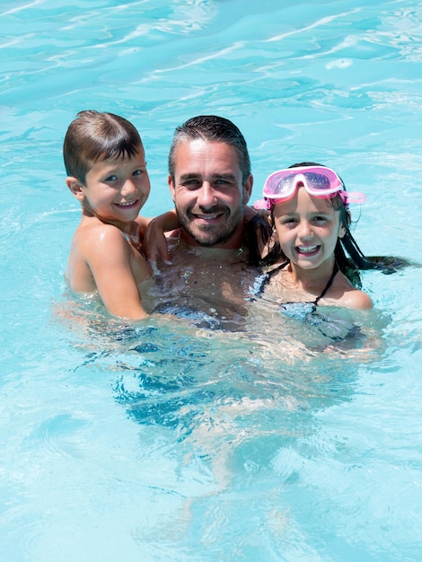 Padre jugando en la piscina con dos niños y niñas