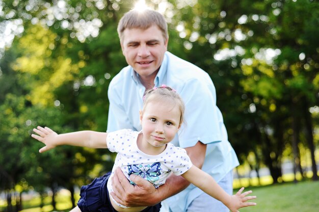 Padre jugando con su hija en el parque sobre un fondo de árboles