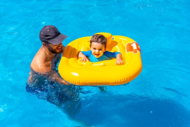 Padre jugando con su hijo con un flotador amarillo en la piscina en verano