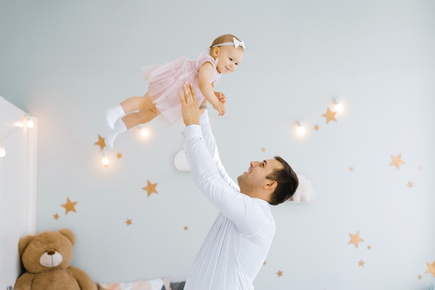 Padre levantando a la niña. Feliz padre levanta y lanza su levantamiento de un niño pequeño. Ambiente hogareño, familia feliz riendo bebé