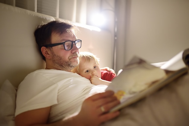 Padre leyendo cuentos para dormir al niño. Papá poniendo a dormir a su hijo