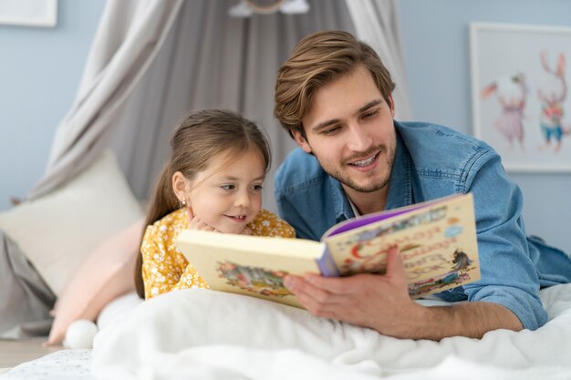 Padre leyendo un libro a su hija mientras está acostado en el suelo en el dormitorio.