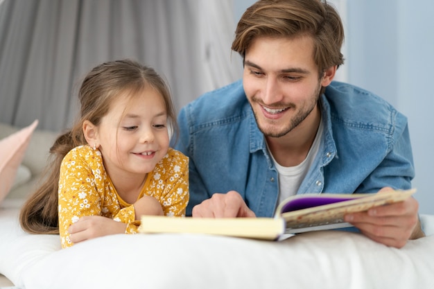 Padre leyendo un libro a su hija mientras está acostado en el suelo en el dormitorio.