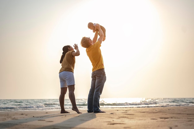 El padre lleva y juega con el hijo del bebé y la madre que se divierten en la playa al atardecer en vacaciones. Familia, playa, relax, hijo, bebé, concepto de estilo de vida.