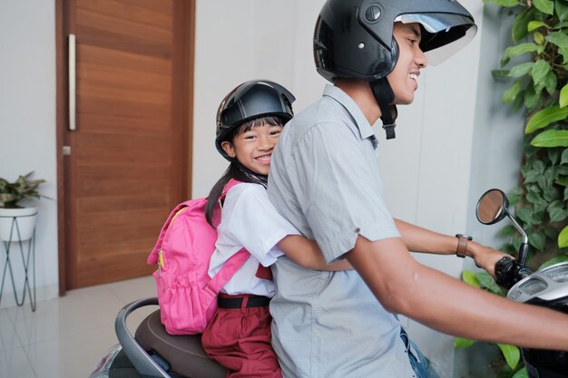 Padre llevando a su hija a la escuela en motocicleta por la mañana. estudiante de primaria asiática vistiendo uniforme de regreso a la escuela