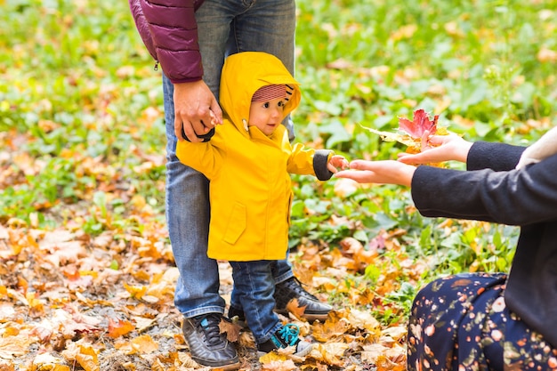 Padre, madre e hijo caminando. Bebé dando los primeros pasos con la ayuda del padre en el jardín de otoño de la ciudad