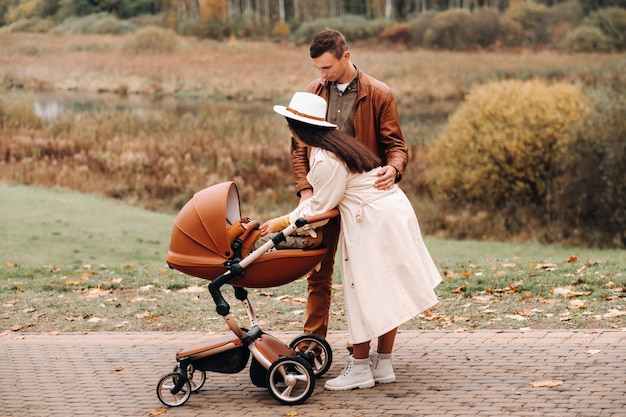 Padre y madre en un paseo con un cochecito en el parque de otoño