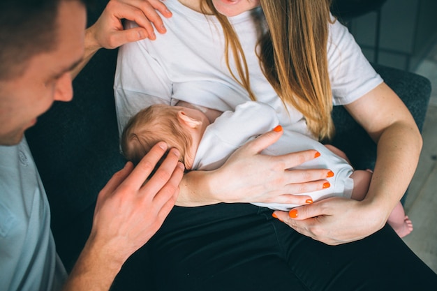 Padre y madre en una sala de estar con un bebé recién nacido. El primer año de vida. Cuidado y salud. Mamá sostiene a un niño pequeño y papá está sentado a su lado. Concepto de primer plano.