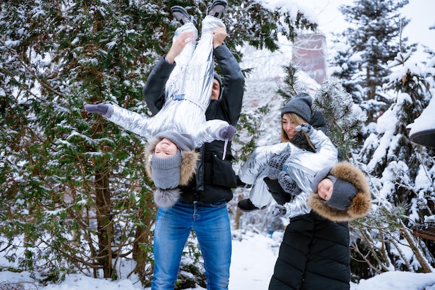 Padre y madre sostienen a los niños en sus brazos riendo alegremente paseo de invierno familiar en el bosque raisi ...