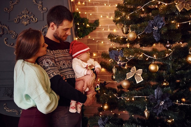 Padre y madre con su hijo juntos en la habitación decorada de Navidad.