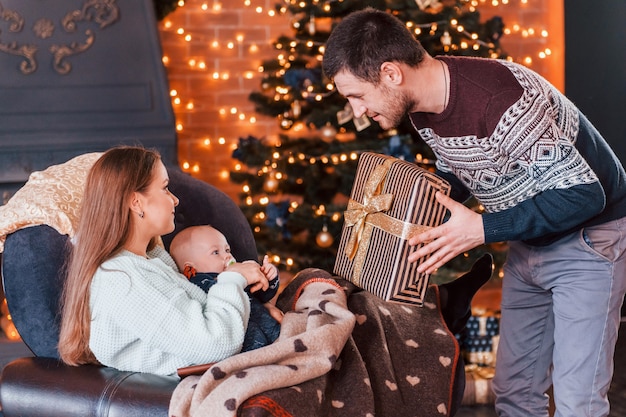 Padre y madre con su hijo juntos en la habitación decorada de Navidad.