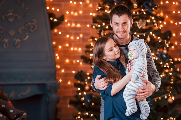 Padre y madre con su hijo juntos en la habitación decorada de Navidad.