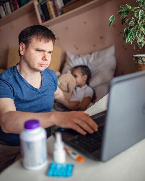 Padre mirando la pantalla del portátil y consultando con un médico en línea en casa