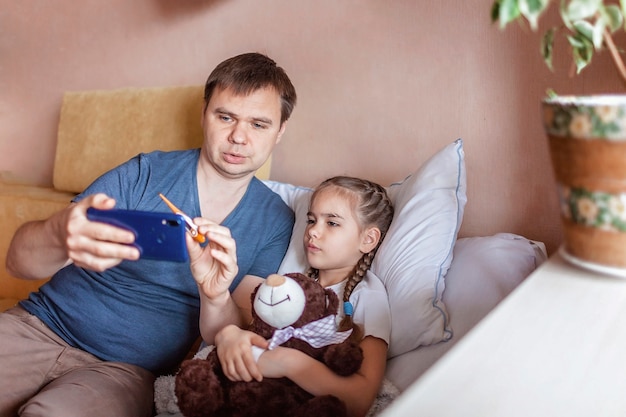 Padre mirando la pantalla del teléfono inteligente y consultando con un médico en línea en casa