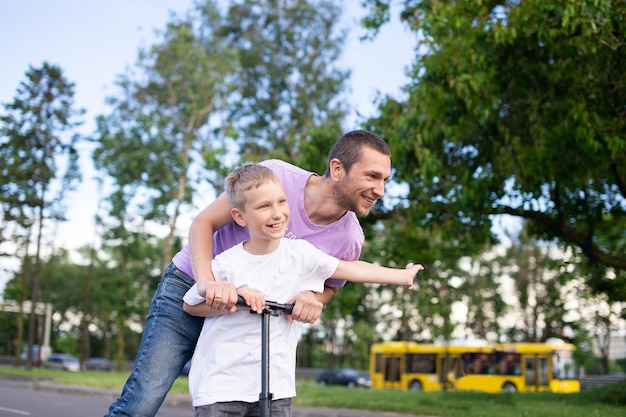 Un padre monta a su hijo con una camiseta blanca en un scooter, el niño feliz extendió las manos