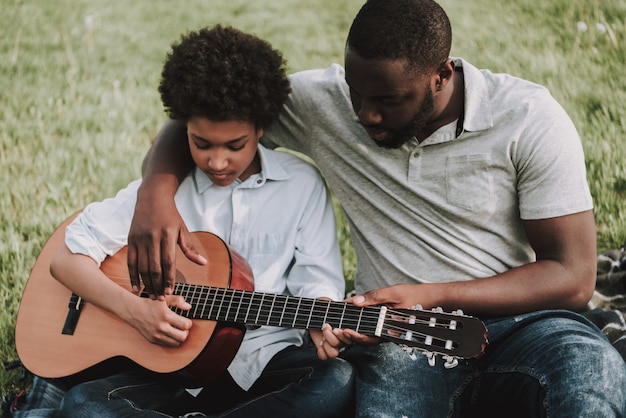 Padre mostrando lecciones para tocar en guitarra a hijo