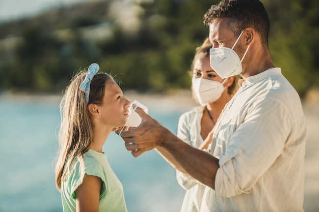 Padre mostrando a su hija adolescente cómo usar correctamente una mascarilla protectora durante la pandemia del coronavirus.