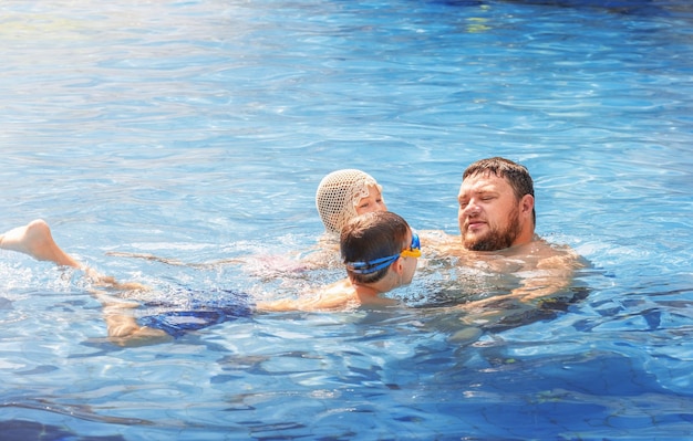 Padre nada en la piscina con dos hijos