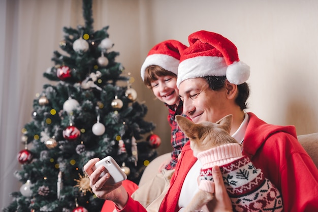 Padre con niño y cachorro con gorro de Papá Noel con teléfono celular