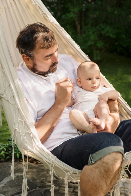 Padre con niño en hamaca relleno agradable y tierno, paternidad. Lindo hijo pequeño en el regazo de papá