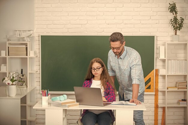 El padre y el niño nerd estudian en la escuela con una computadora portátil en el estudio de fondo de la pizarra