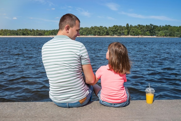 Padre con un niño en el terraplén junto al río la vista desde atrás