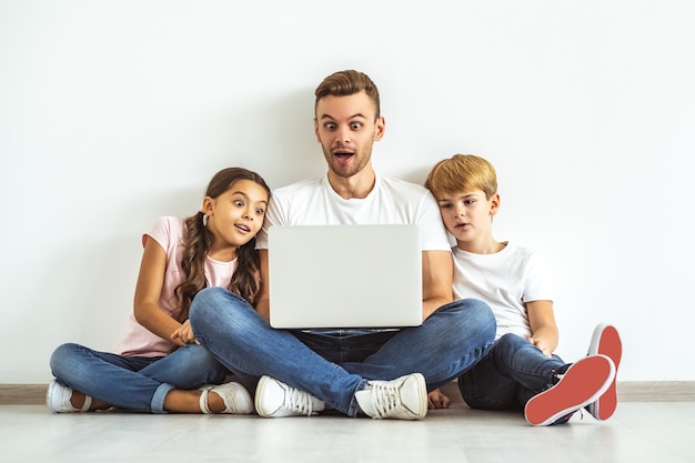 El padre y los niños con una computadora portátil sentados en el suelo.