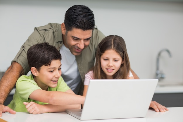 Padre con niños pequeños usando la computadora portátil en la cocina