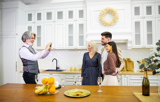 Padre de pelo gris tomando una foto de su esposa y su hijo y su hija en la elegante cocina de casa