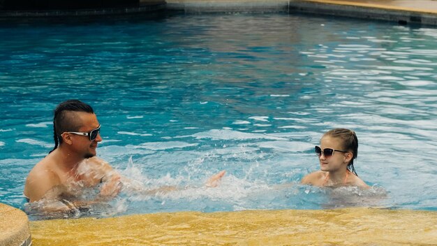 El padre con la pequeña hija se divierte en la piscina Papá juega con el niño La familia disfruta de las vacaciones de verano en una piscina saltando girando agua salpicada Cámara lenta