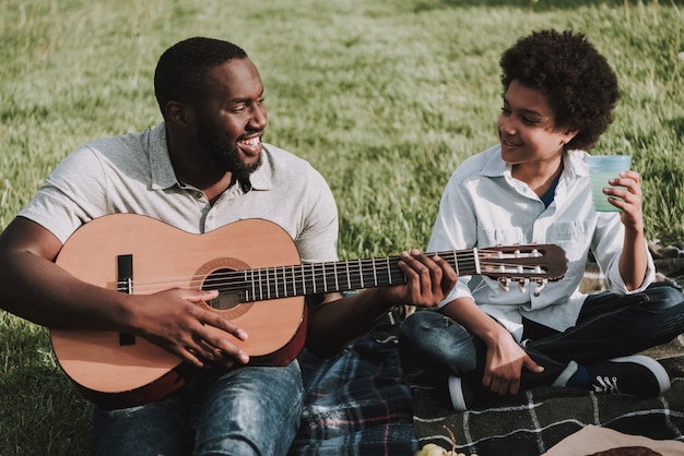 Foto padre play en guitarra y looking on son en picnic.