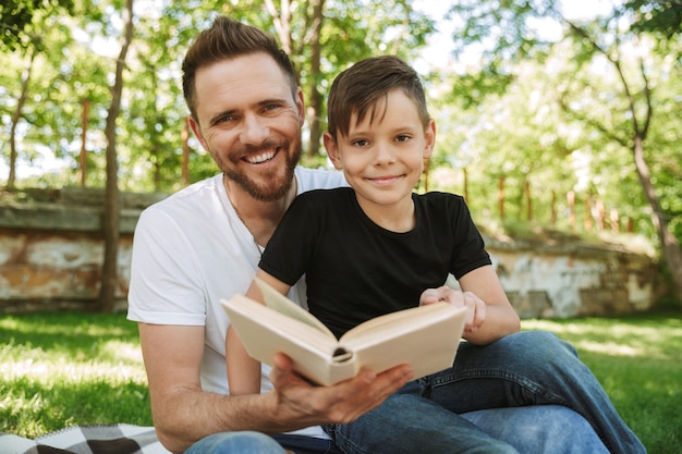 Padre sentado con su pequeño hijo al aire libre leyendo el libro.