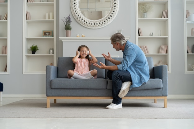 Padre serio regañando a su pequeña hija en el interior de una casa.