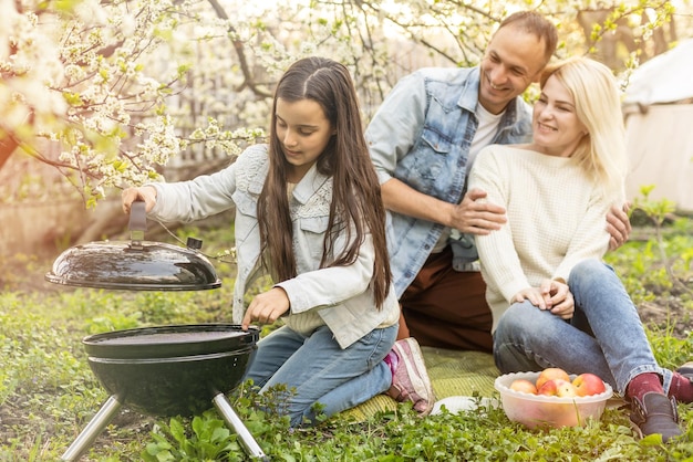 padre sonriente asando carne con su hija en el campamento.