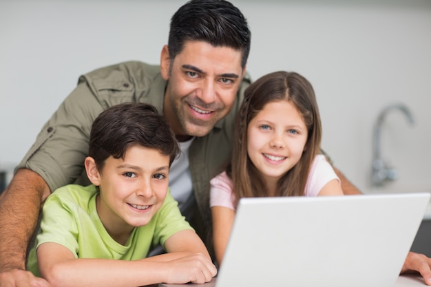 Foto padre sonriente con niños usando la computadora portátil en la cocina