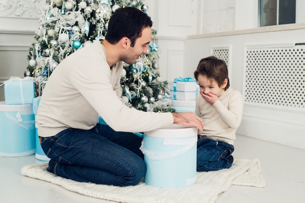 Padre sonriente y su hijo abriendo regalos de Navidad en la sala de estar