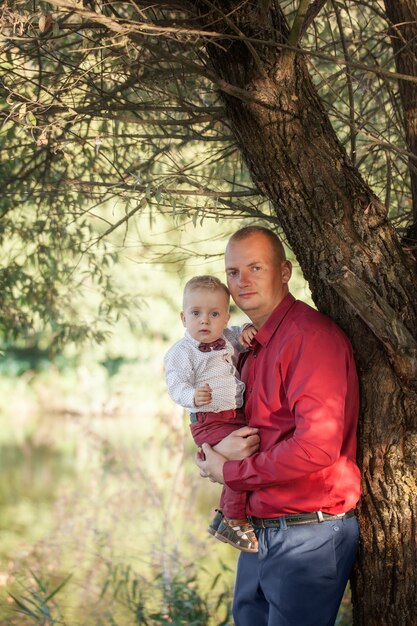 Padre sosteniendo al hijo en sus brazos, divirtiéndose al aire libre en un día soleado de verano