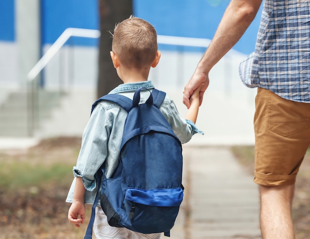 Padre sosteniendo la mano del pequeño hijo con mochila al aire libre. De vuelta a la escuela. Primer día de otoño.