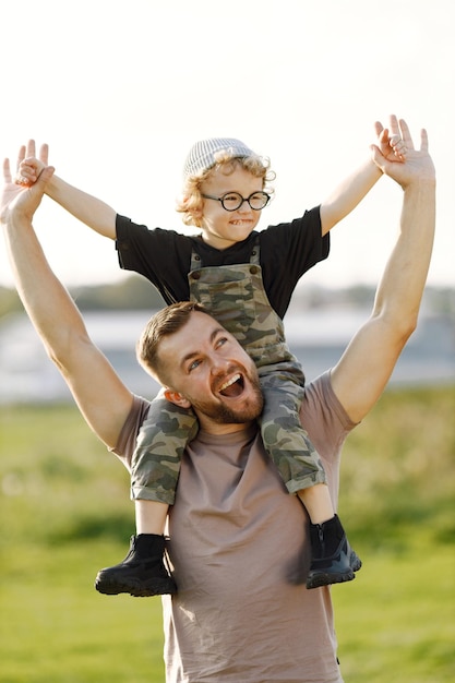 Padre sosteniendo a su hijo sobre los hombros en el parque de verano al aire libre Curly toddler boy vistiendo un color caqui en general