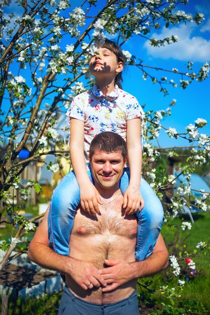 El padre sostiene a la hija sobre los hombros en el exuberante jardín.