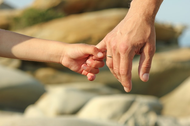 El padre sostiene la mano de un niño pequeño cerca de piedras.