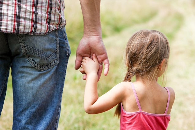 El padre sostiene la mano de un niño pequeño en la naturaleza.