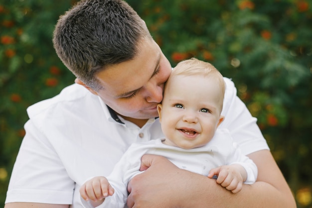 Un padre sostiene a su pequeño hijo en sus brazos y lo besa. el bebé está sonriente y feliz. dia del padre